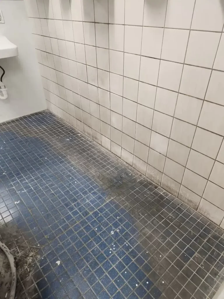 Filthy bathroom tile floor before janitorial scrubbing and wash.