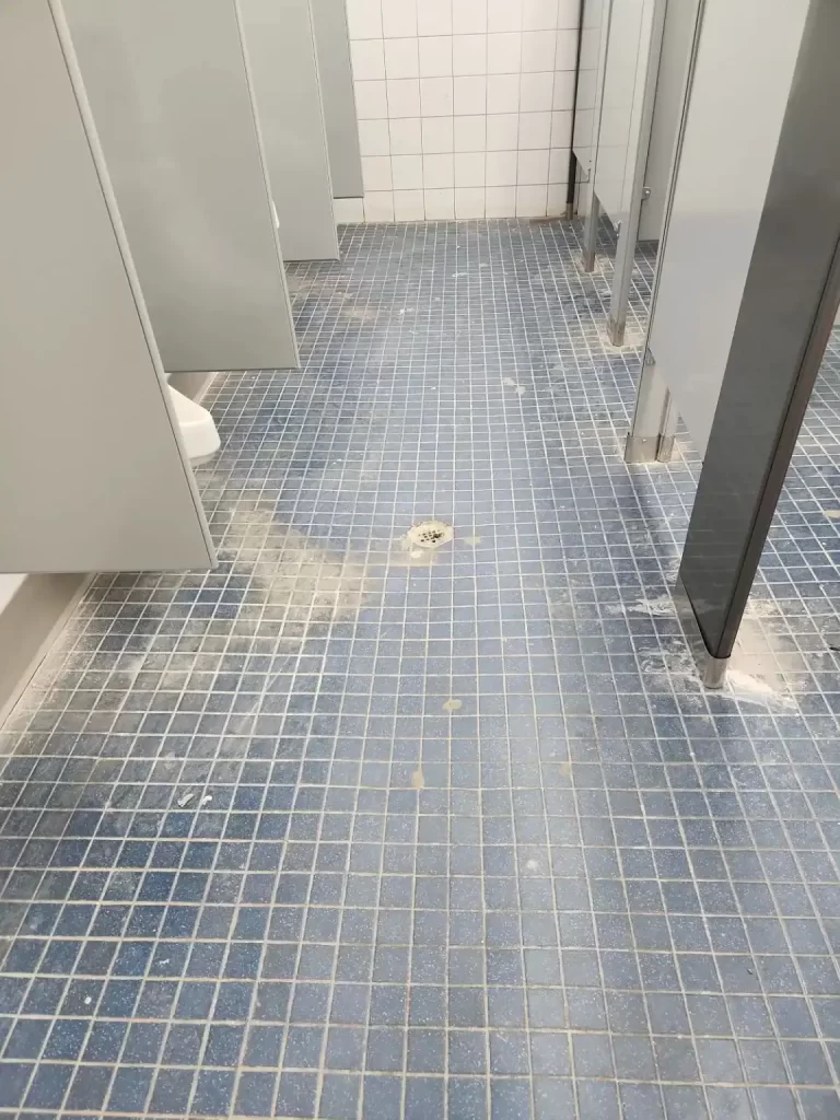 Filthy bathroom tile floor before janitorial scrubbing and wash.