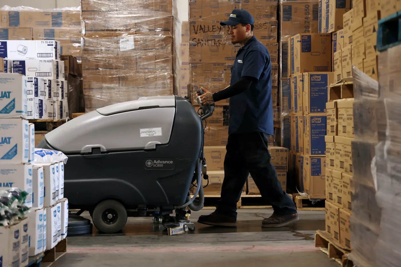 Worker scrubbing concrete floor in industrial warehouse
