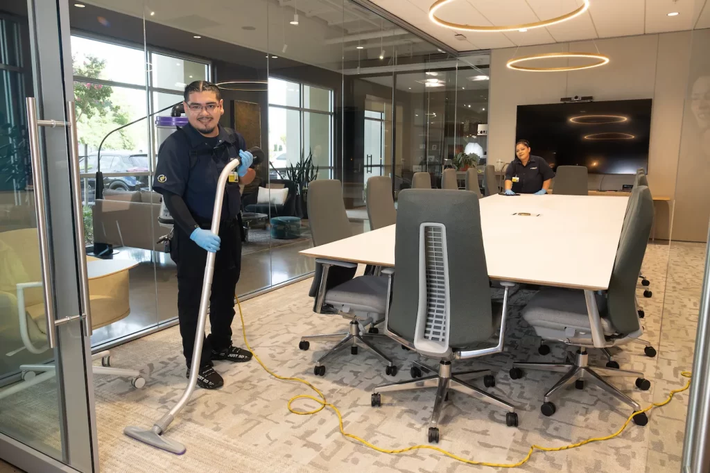 Professional cleaners vacuuming and cleaning a conference room in an office.