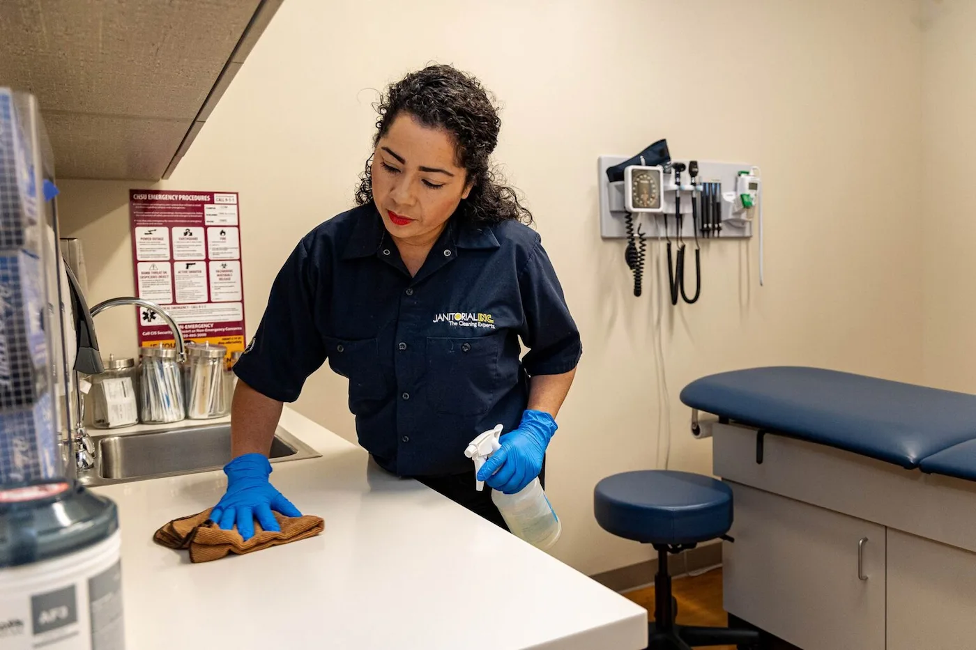 Janitorial woman cleaning surface of a table in a medical room.