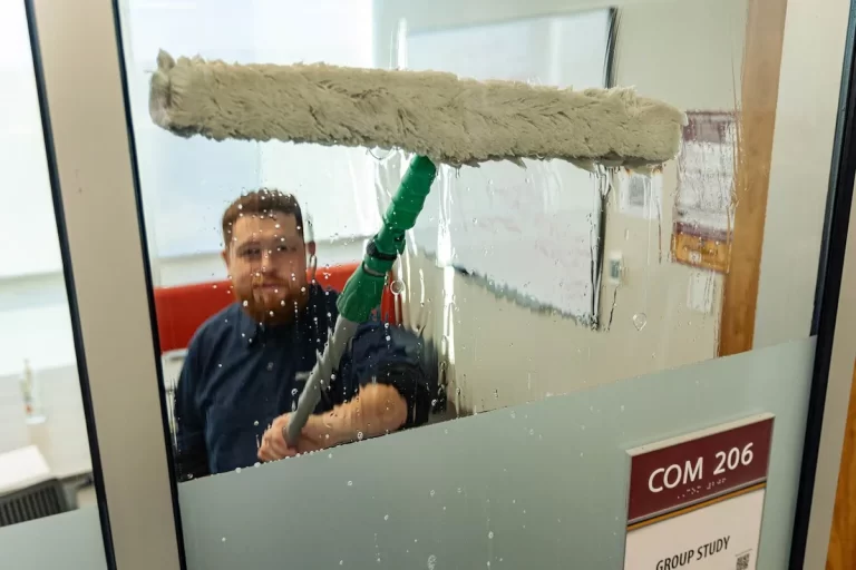 Window washer cleaning an interior window surface in a conference room.