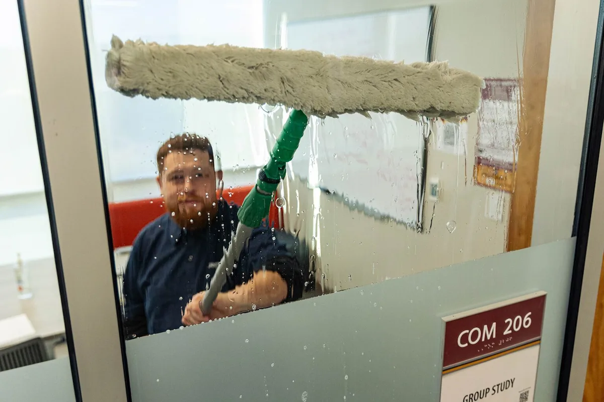 Window washer cleaning an interior window surface in a conference room.